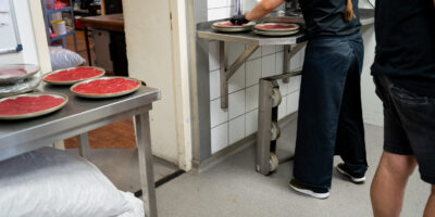 Grijze antislip vloer in horecakeuken waar personeel vlees op borden legt naast een vleessnijmachine