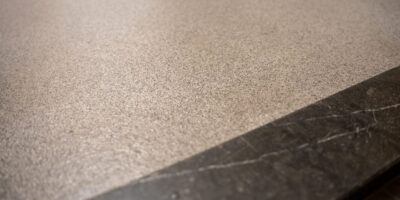 25 jaar ervaring in vloeren voor sanitaire ruimtes Close up van de naadloze overgang tussen beige gietvloer en donkere natuurstenen plint in sanitaire ruimte