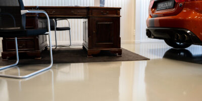 Hoogglans gietvloer in Jaguar showroom met antiek bureau en sportwagen