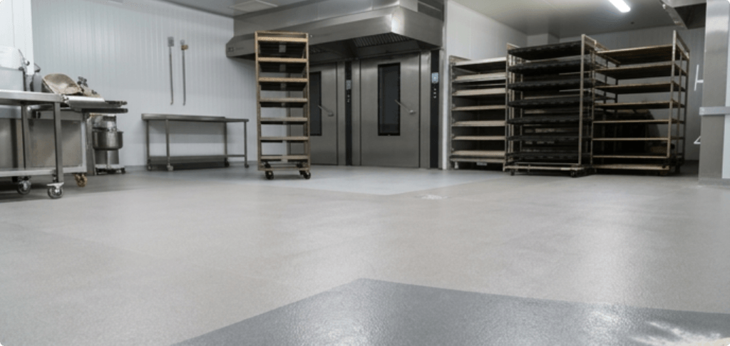 Hygiënische coatingvloer in een bakkerij Interieur van een bakkerij met een naadloze grijze coatingvloer, bakkersrekken op wieltjes en roestvrijstalen werktafels