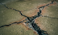 Diepe scheuren in betonvloer van koelcel Close up van een diepe, kruisvormige scheur in een groenige betonvloer in een koelcel, met ijskristallen in de opening