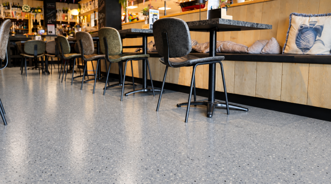 Gietvloer in gezellig café-interieur Grijze gietvloer met terrazzo-look in café met houten bar en visthema
