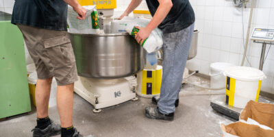 DuraQuartz vloer in actieve bakkerijproductie DuraQuartz vloer in bakkerij bij Kemper deegmixer met twee medewerkers die meel toevoegen.
