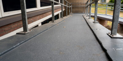 Close-up van vernieuwde hellingbaan met leuningen tussen gebouwen.