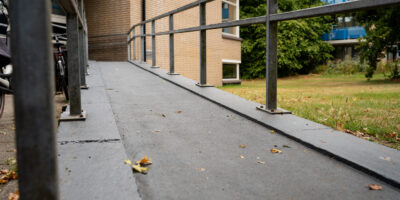 Vernieuwde hellingbaan met leuning langs gebouw en groen grasveld.