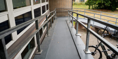 Overzicht van vernieuwde hellingbaan met leuningen, gebouw en fietsen op de achtergrond.