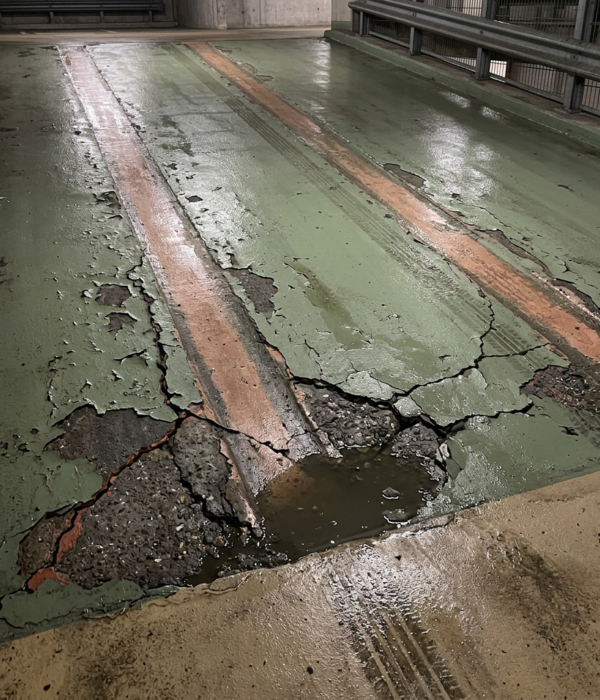 Schade aan coating van een hellingbaan Ernstig beschadigde coating op hellingbaan in parkeergarage met scheuren en loszittende delen.
