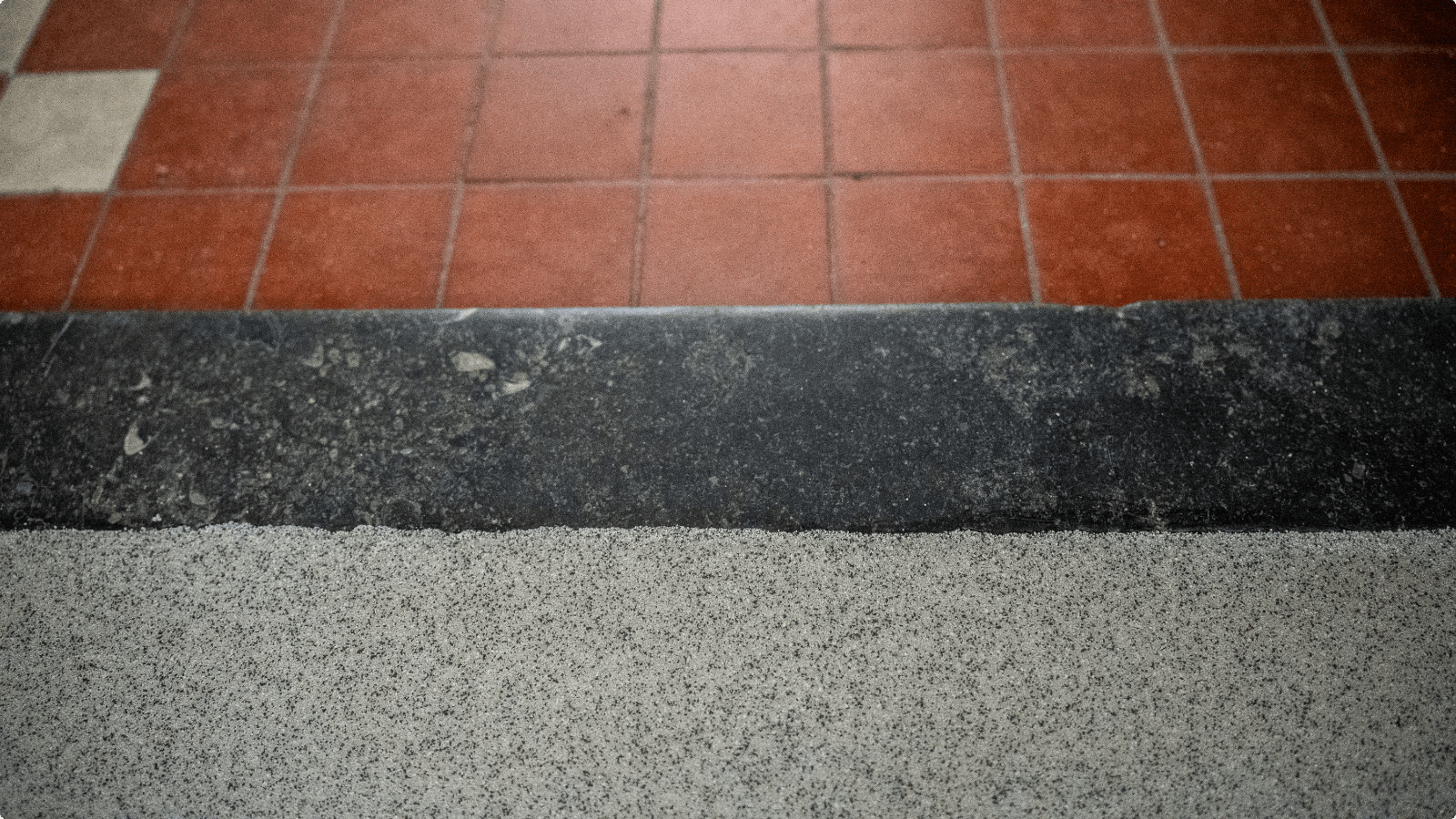 Overgang van een rode tegelvloer via een zwarte drempel naar een lichte gietvloer