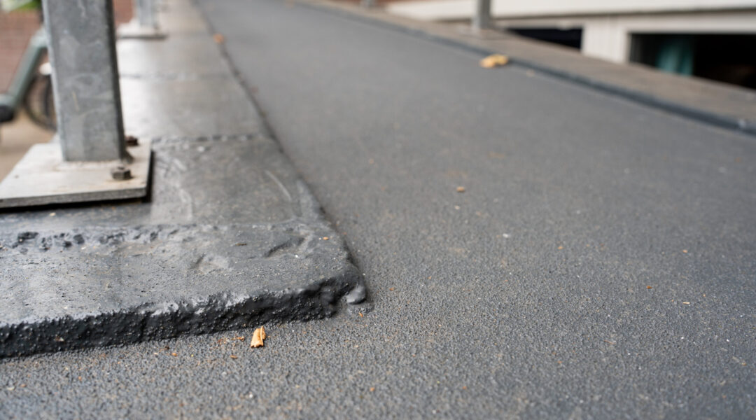 Antraciet DuraQuartz Outdoor vloer met antislip structuur op een buitenhelling, strak afgewerkt rond de voetplaten van een stalen leuning.