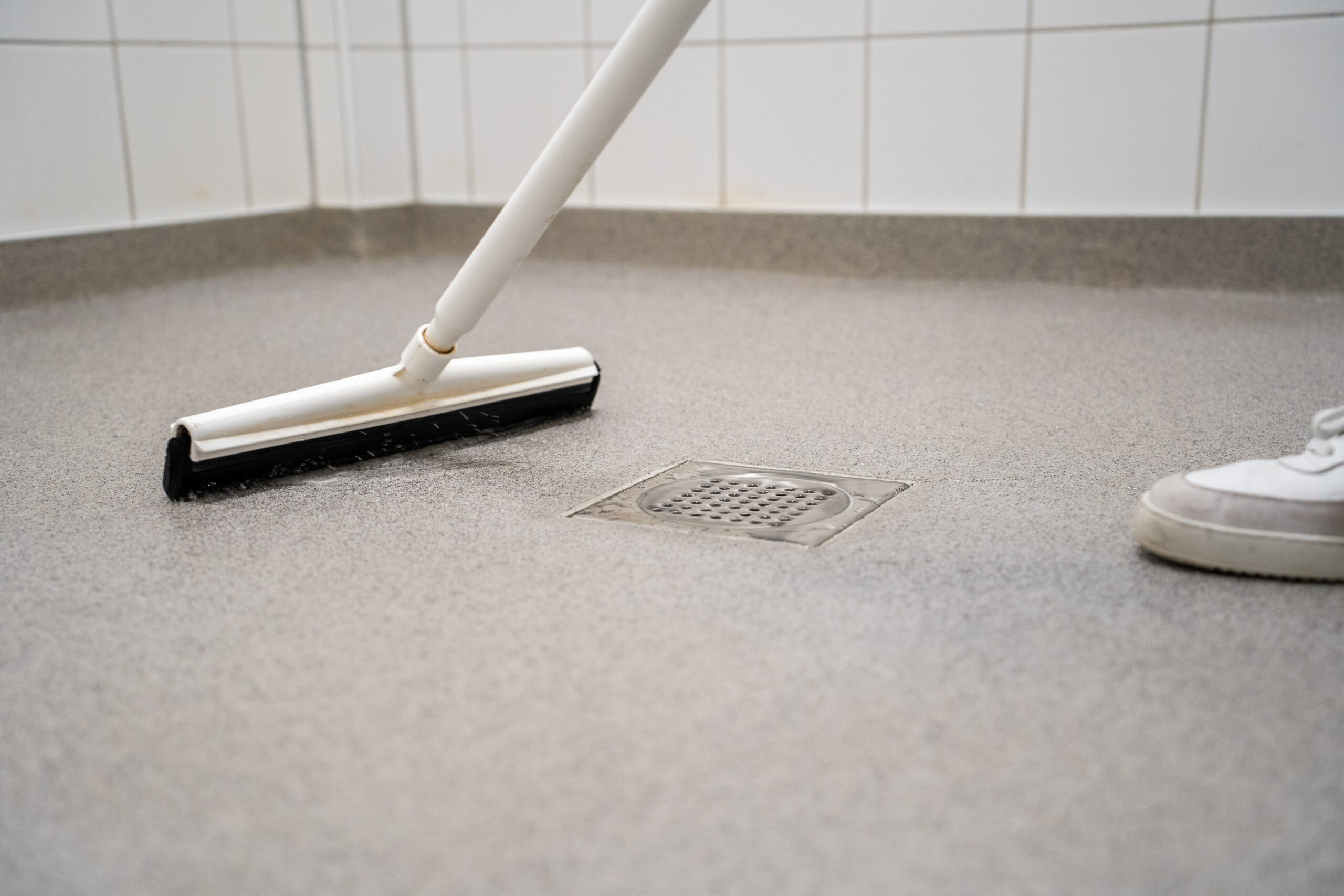 Vloertrekker naast een vloerput op een grijze gietvloer tijdens het schoonmaken