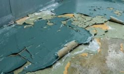 Volledig loslatende coating op koelcelvloer Groenblauwe coating op koelcelvloer die in grote krullende vellen loslaat en meerdere onderliggende kleurlagen blootlegt
