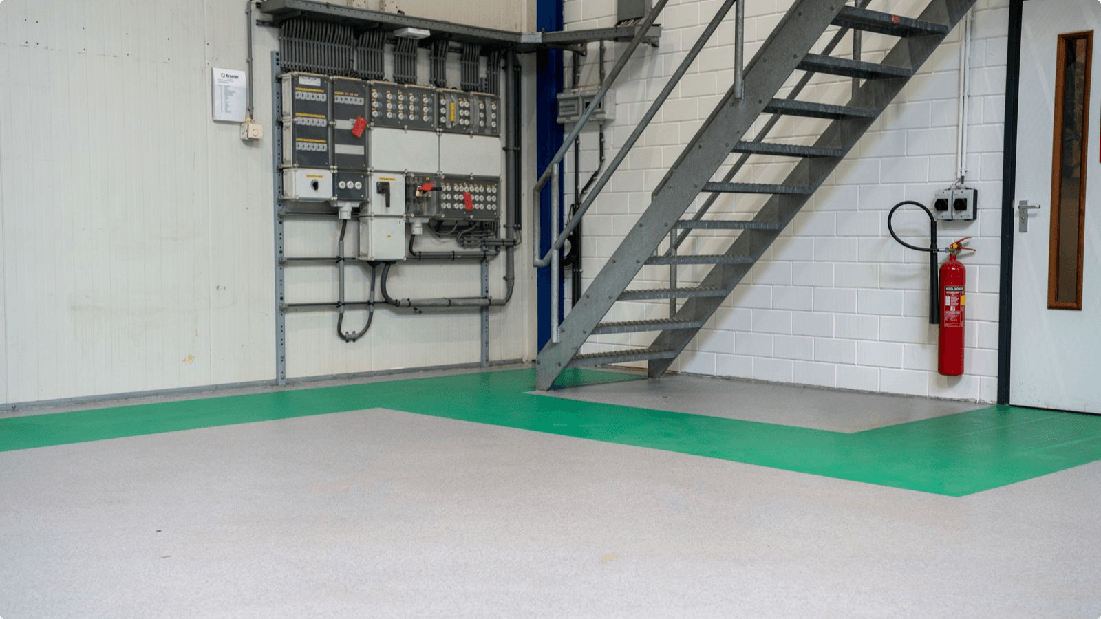 Grijze DuraQuartz troffelvloer met groene looproutes bij de trap in de werkplaats van Distrimex