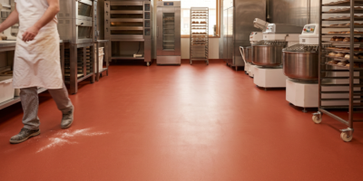 Bakker loopt over gave rode vloer in productiebakkerij Bakker in werkkleding loopt over strakke rode gietvloer tussen ovens, mixers en broodrekken in professionele bakkerij