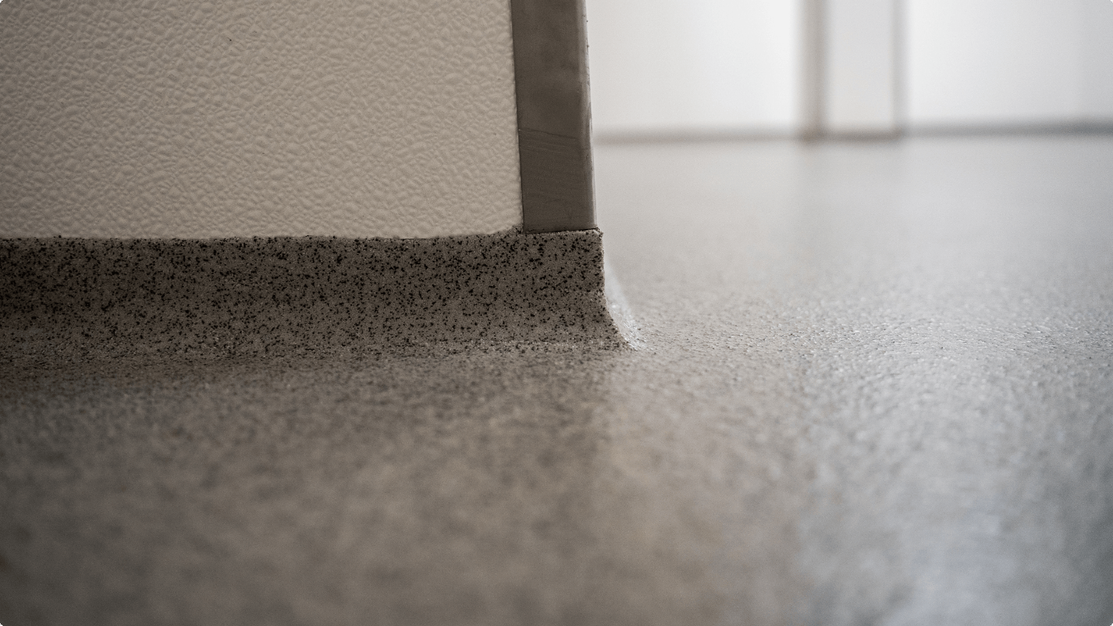 Gietvloer met naadloze opstaande plint tegen de wand, afgewerkt met aluminium hoekprofiel