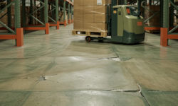Ongelijke vloerplaten in magazijngangpad Groenige magazijnvloer met verzakte, ongelijke vloerplaten en scheuren, met een elektrische pallettruck en stellingen