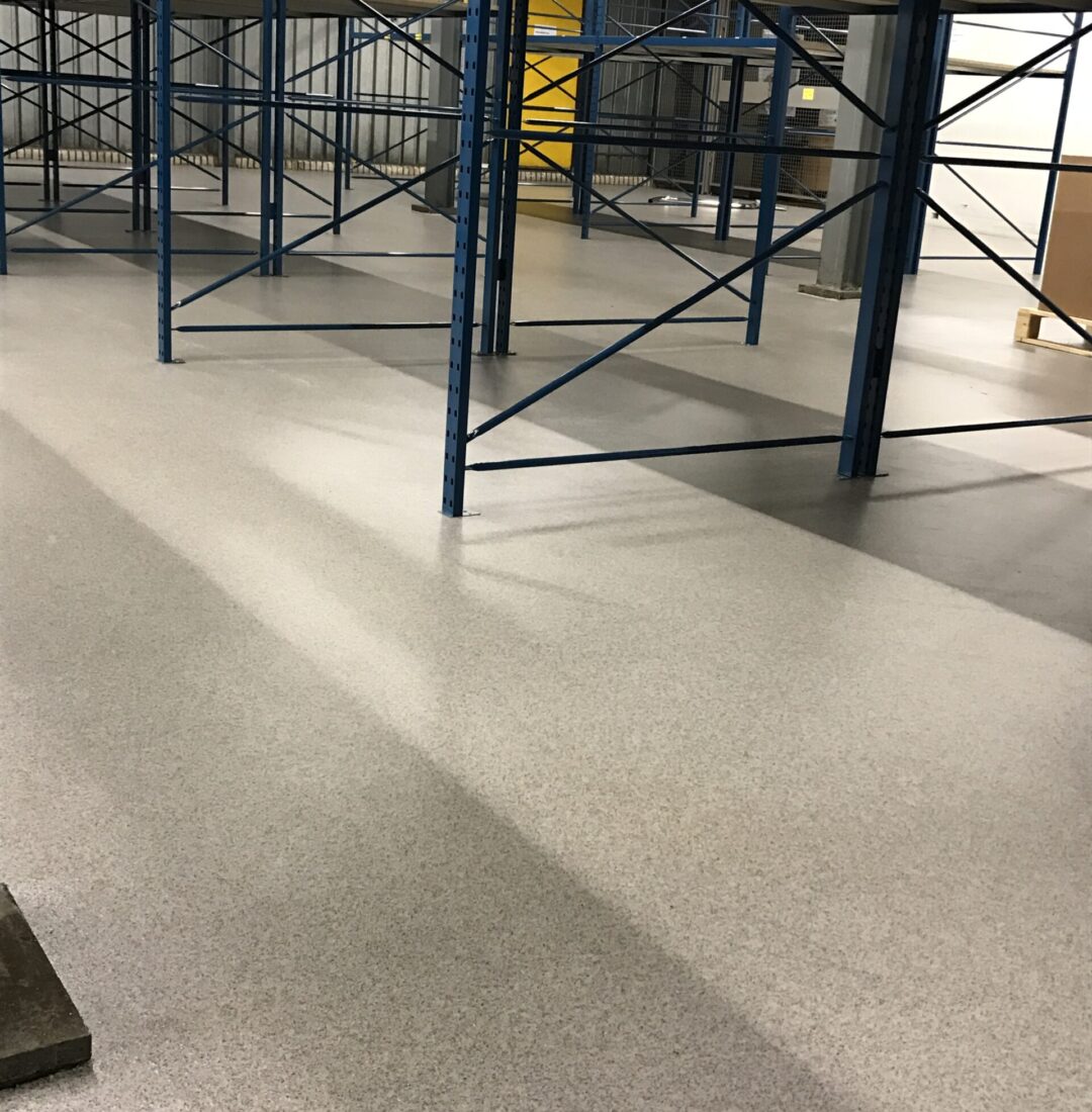 Bedrijfsvloer magazijn na oplevering Afgewerkte gietvloer in magazijn met blauwe opslagstellingen