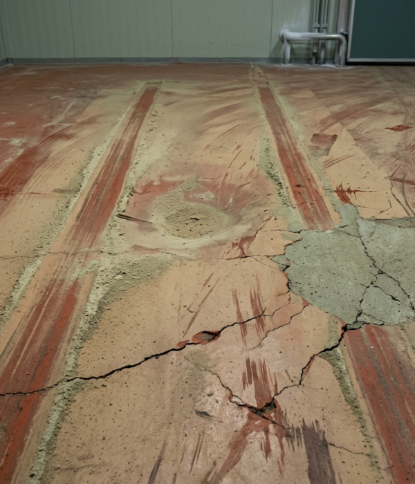 Scheuren, sleepsporen en gaten in magazijnvloer Verweerde magazijnvloer met bandensporen, een uitgesleten kuil en een grote scheur met afgebrokkeld beton