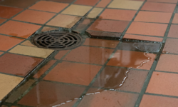 Terracotta en oker tegelvloer in keuken met ronde afvoerput waarnaast een plas water blijft staan