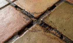 Terracotta en olijfgroene vloertegels in keuken met sterk vervuilde, uitgesleten voegen op het kruispunt