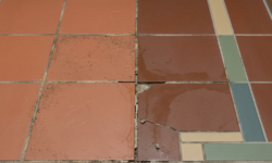 Gebarsten decoratieve tegelvloer in sanitaire ruimte Terracotta tegelvloer met blauwgroene en beige accentlijnen in sanitaire ruimte, met een gebarsten en verkleurde tegel