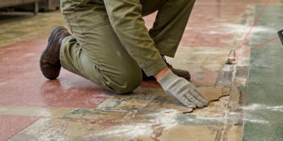 Vloerinspectie bij beschadigde bakkerijvloer Vloerinspecteur in werkkleding onderzoekt beschadigde terrazzo bakkerijvloer, met laserafstandsmeter erbij